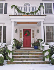 wreath with a bow on exterior door, framed by garland wrapped around railing and pillars