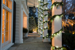 garland and string lights wrapped around evergreen tree and pillars, illuminated at dusk